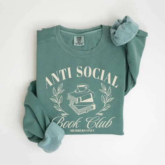 A folded unisex Comfort Colors sweatshirt in light green color, featuring 'Anti Social Book Club - Members Only' text and book stack design in cream color