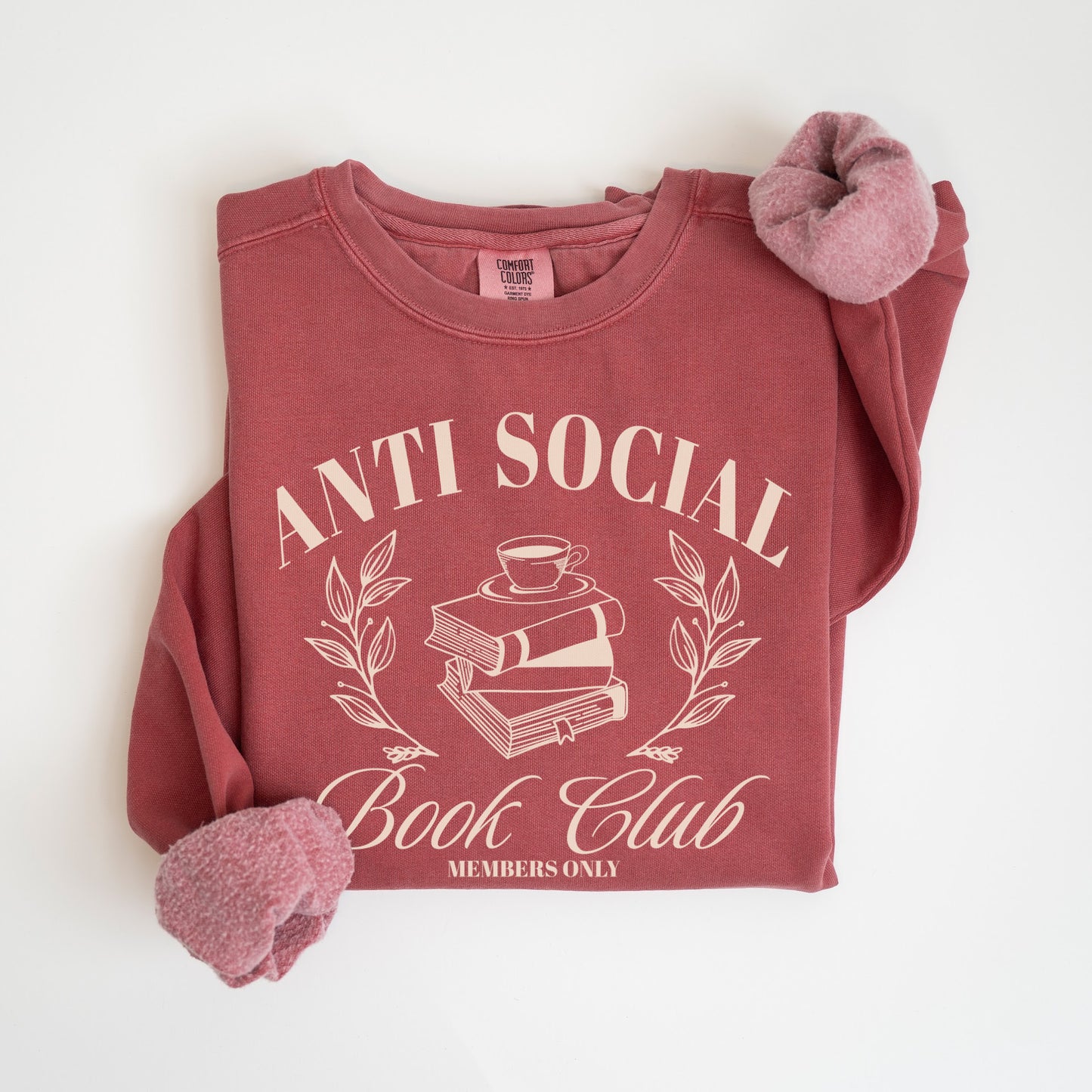 A folded unisex Comfort Colors sweatshirt in crimson color, featuring 'Anti Social Book Club - Members Only' text and book stack design in cream color