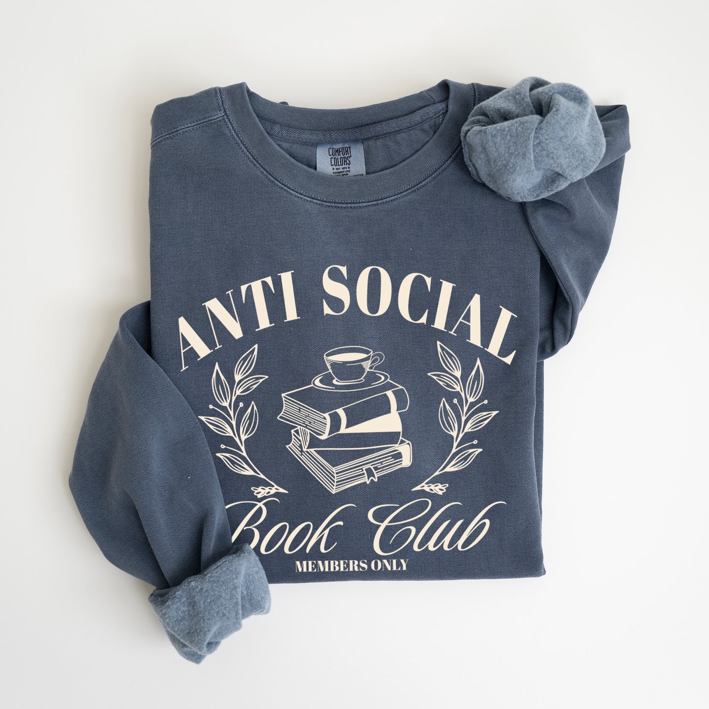 A folded unisex Comfort Colors sweatshirt in denim color, featuring 'Anti Social Book Club - Members Only' text and book stack design in cream color