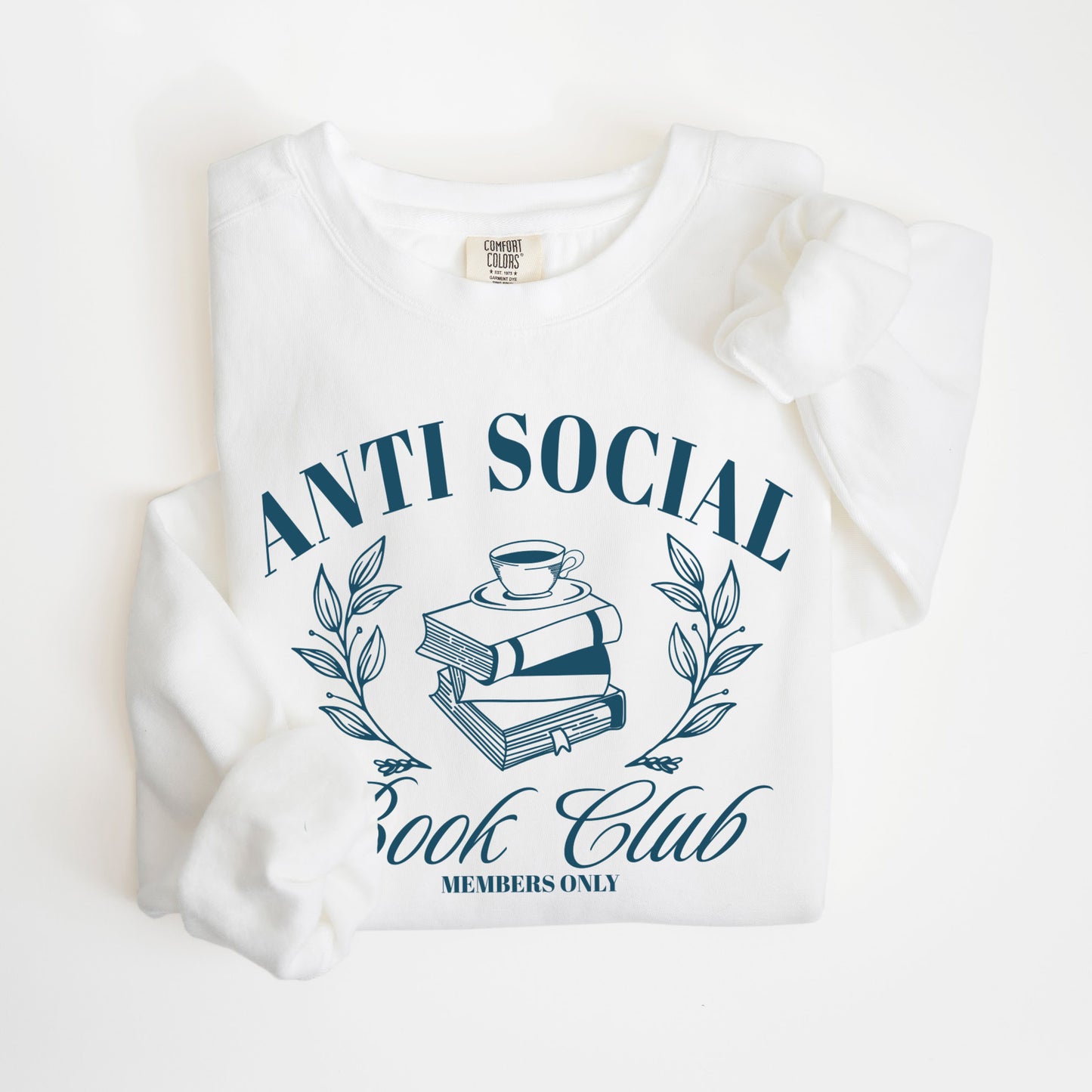 A folded unisex Comfort Colors sweatshirt in white color, featuring 'Anti Social Book Club - Members Only' text and book stack design in dark teal color