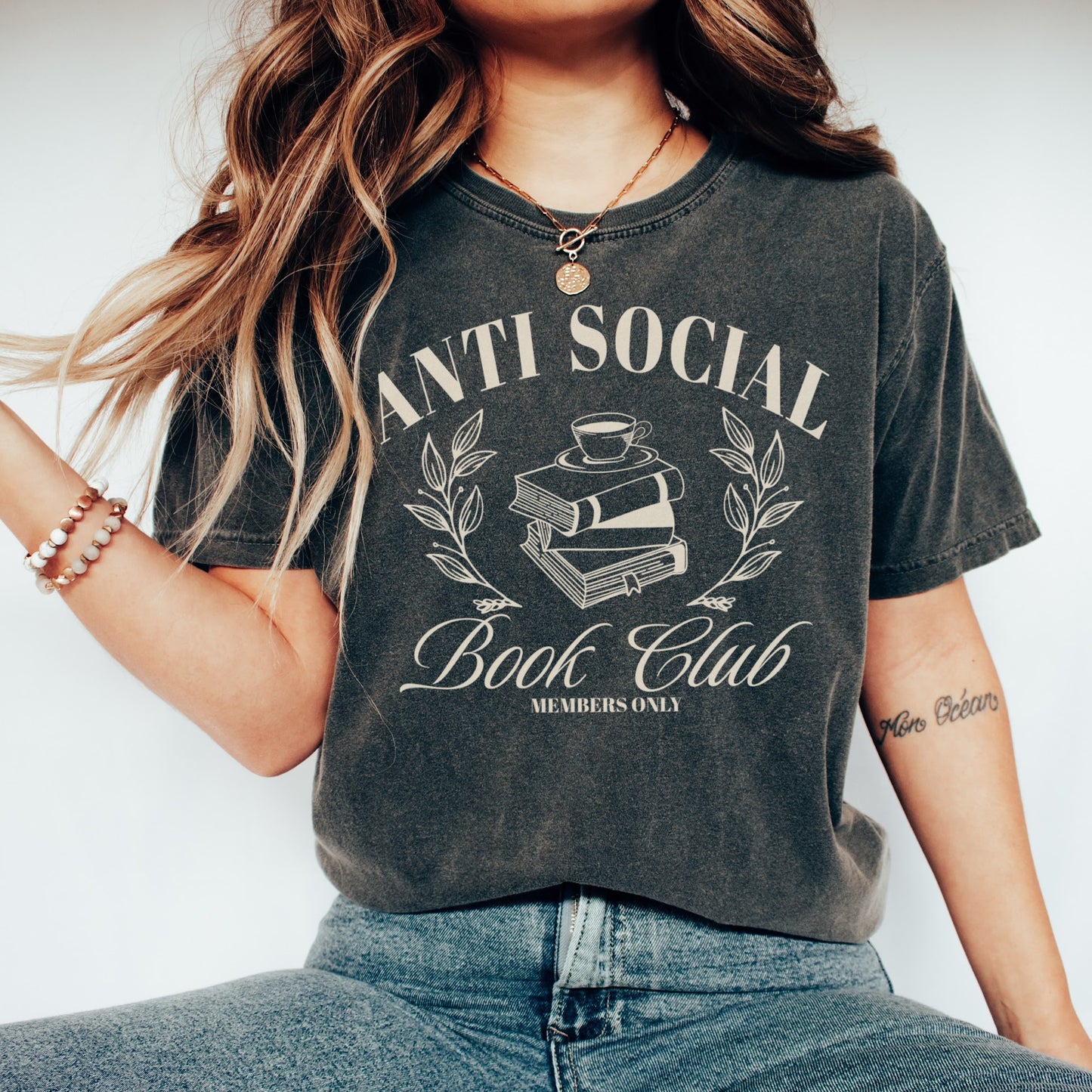 A woman wearing a unisex Comfort Colors Shirt in the color pepper.The design on the shirt features 'Anti Social Book Club - Members Only' text and book stack design in cream color