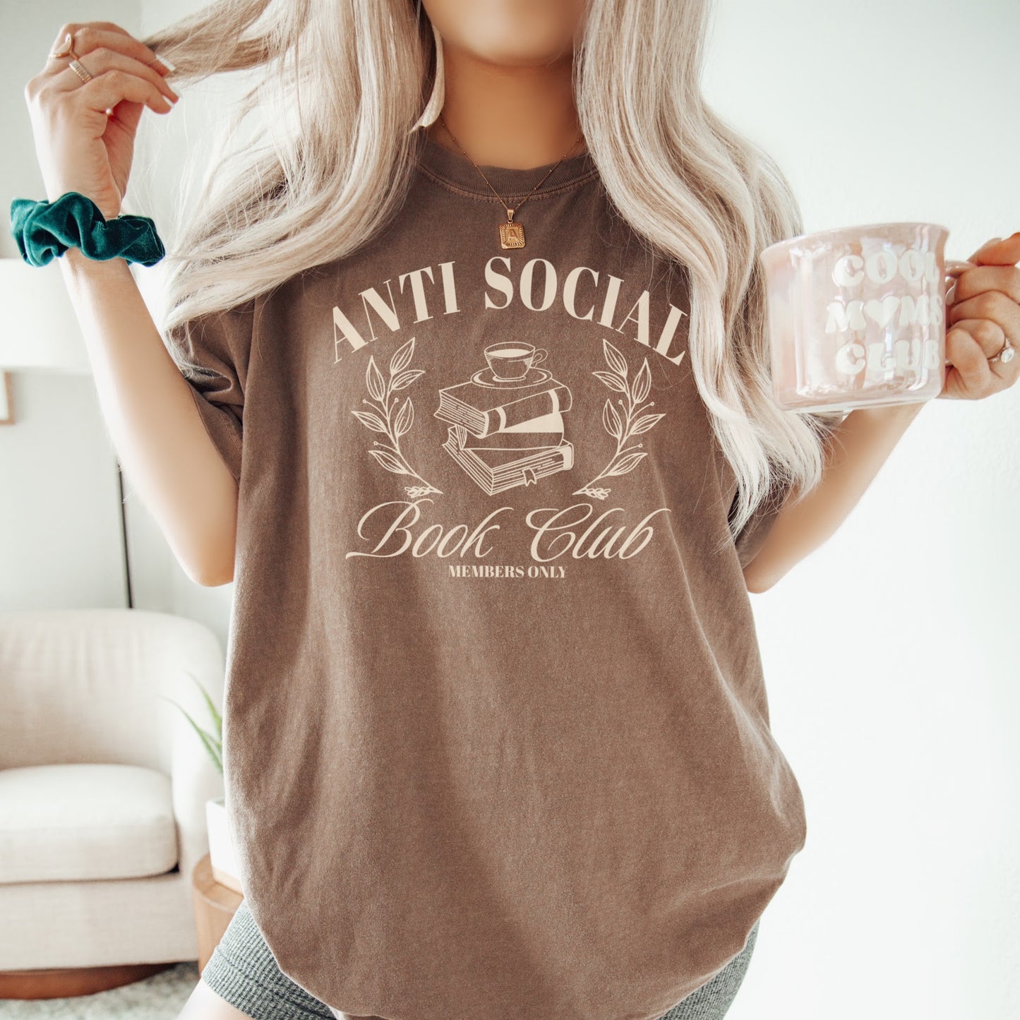 A woman wearing a unisex Comfort Colors Shirt in the color espresso.The design on the shirt features 'Anti Social Book Club - Members Only' text and book stack design in cream color