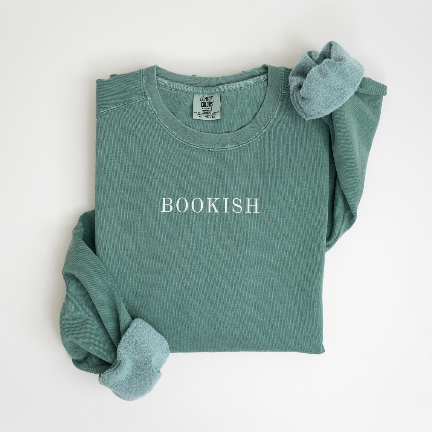 A folded unisex Comfort Colors sweatshirt in light green color with the word 'BOOKISH' printed in a simple, classic font on the front.