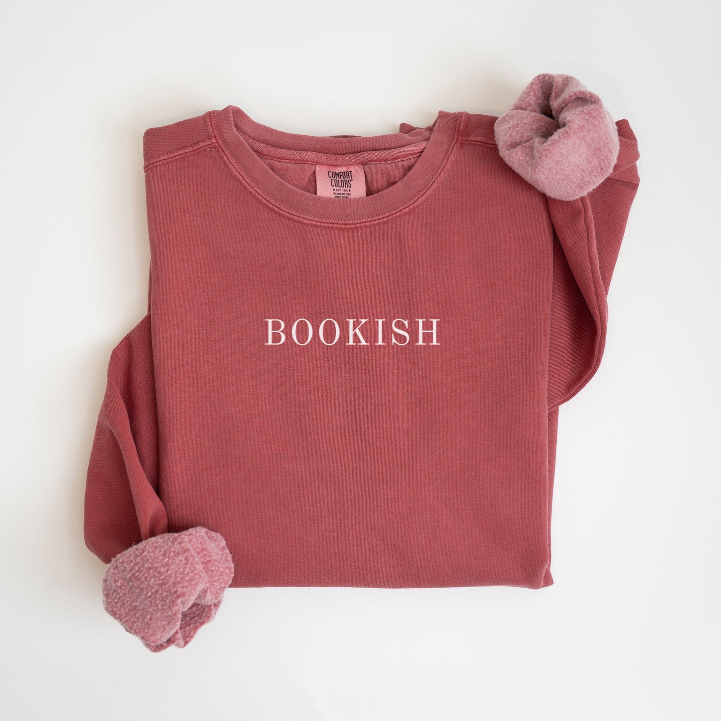 A folded unisex Comfort Colors sweatshirt in crimson color with the word 'BOOKISH' printed in a simple, classic font on the front.