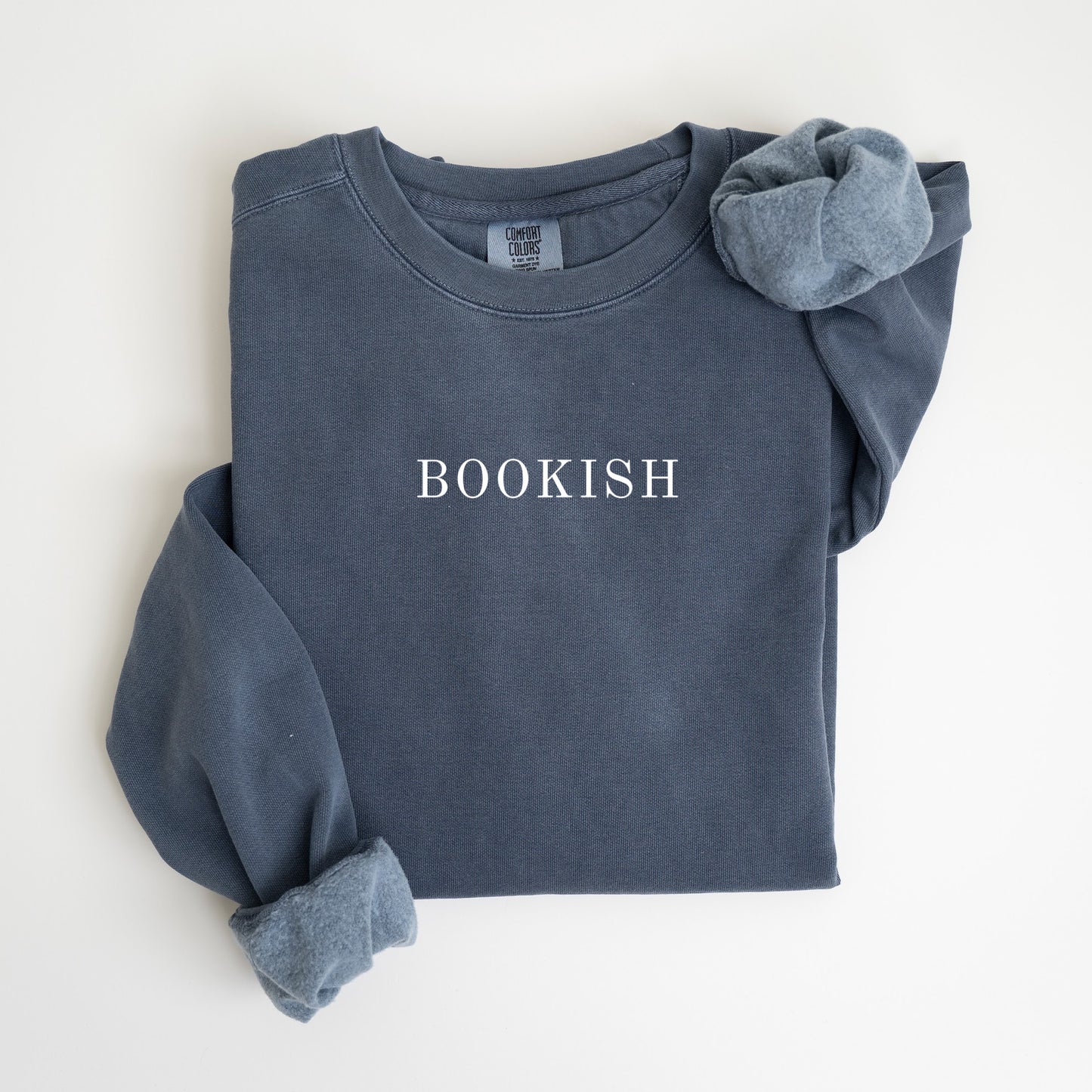 A folded unisex Comfort Colors sweatshirt in denim color with the word 'BOOKISH' printed in a simple, classic font on the front.
