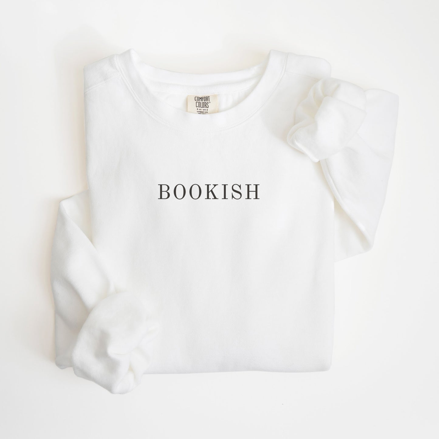 A folded unisex Comfort Colors sweatshirt in white color with the word 'BOOKISH' printed in a simple, classic font on the front.