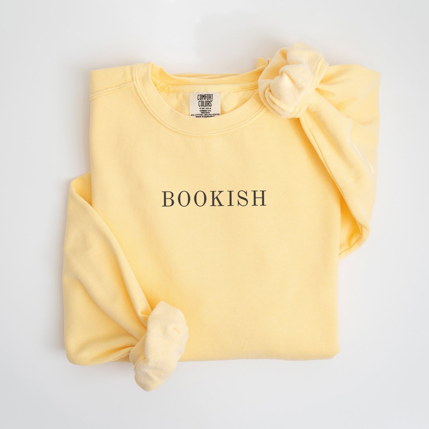 A folded unisex Comfort Colors sweatshirt in butter color with the word 'BOOKISH' printed in a simple, classic font on the front.