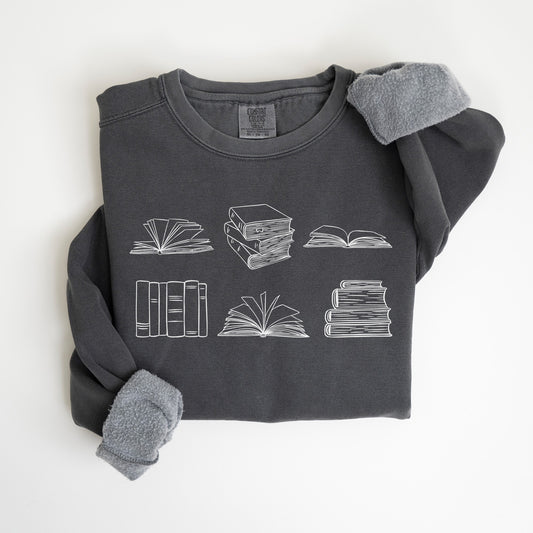 A folded unisex Comfort Colors sweatshirt in pepper color, featuring white line drawings of various book illustrations, including open and stacked books.