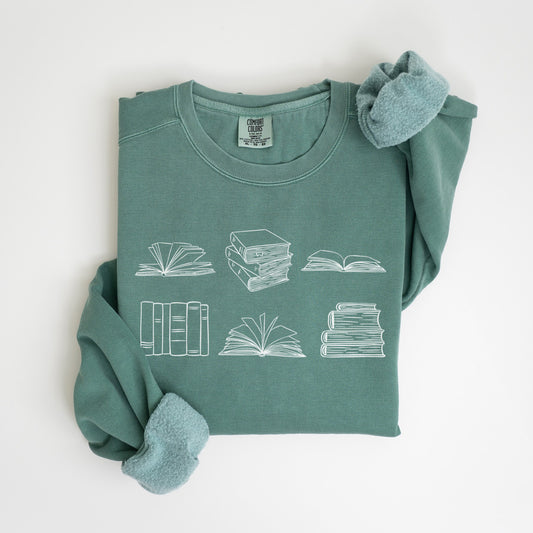 A folded unisex Comfort Colors sweatshirt in light green color, featuring white line drawings of various book illustrations, including open and stacked books.