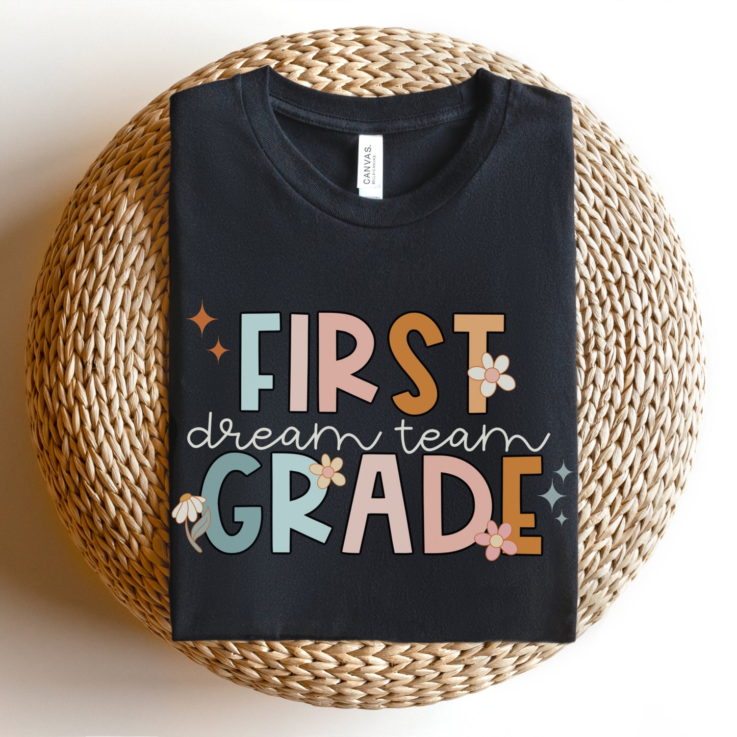 "First Grade Dream Team" with bright, multicolored font and cursive lettering. Random star and flower elements places around design.Unisex women's Tshirt, color: Black