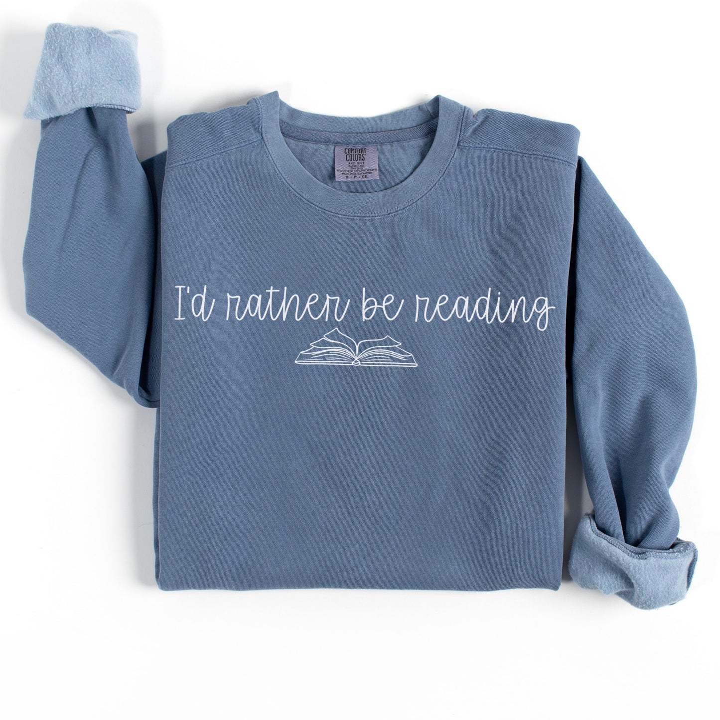 A folded unisex Comfort Colors sweatshirt in blue jean with the phrase 'I'd rather be reading' printed above a simple line drawing of an open book.