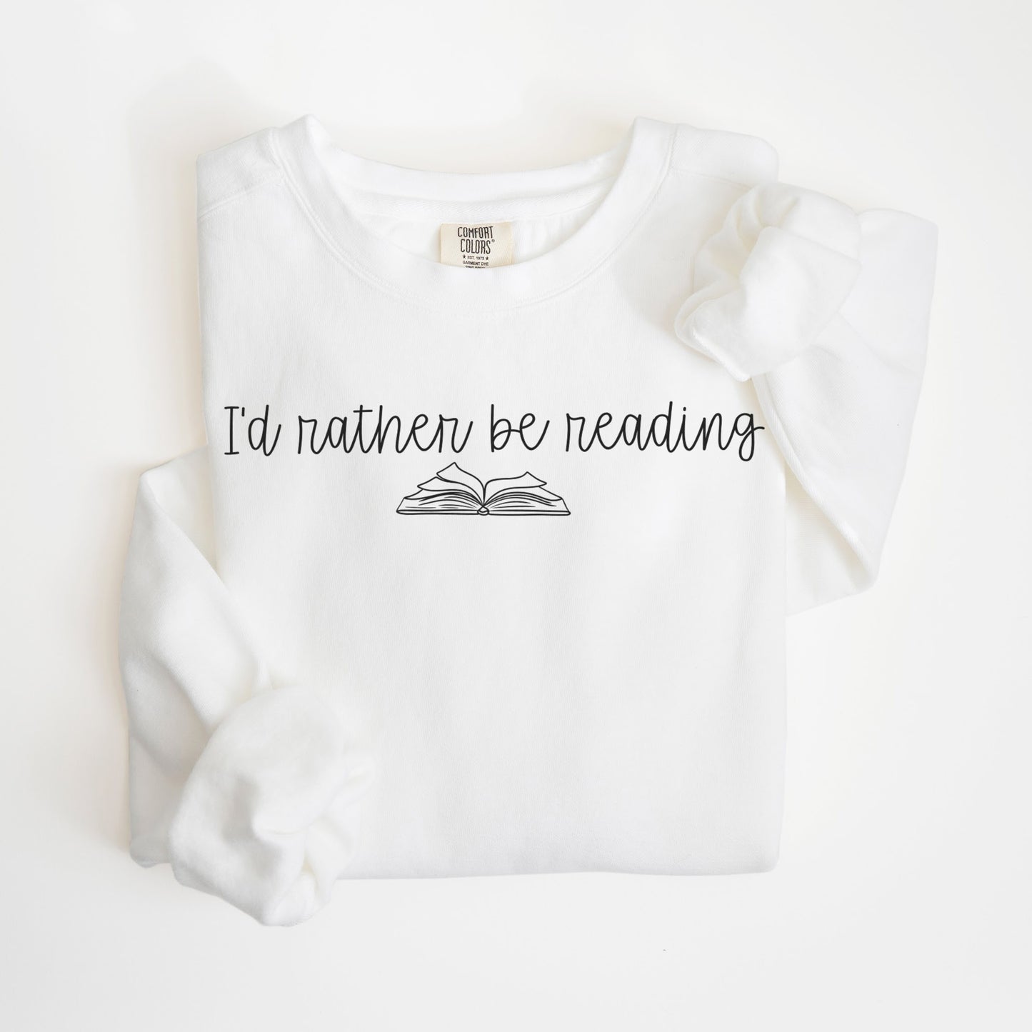 A folded unisex Comfort Colors sweatshirt in white with the phrase 'I'd rather be reading' printed above a simple line drawing of an open book.