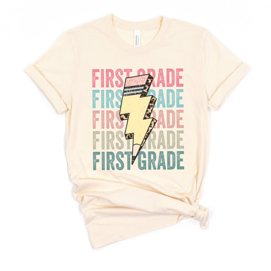 "First grade" repeated 5 lines in a row. Each Line a different color with a lightning bolt shaped pencil with cheetah accents in the center on top of 'first grade'. Unisex women tshirt Color:Natural