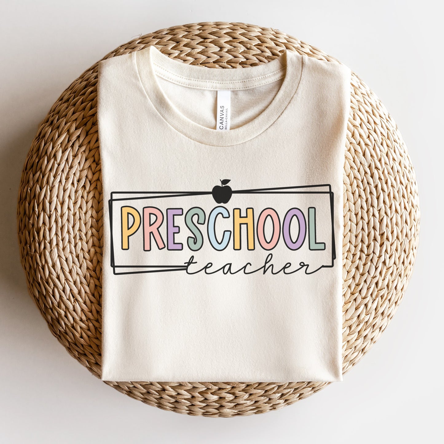 Preschool Teacher Tshirt Multicolor font with white rectangle borders and an apple on the top. Natural Color