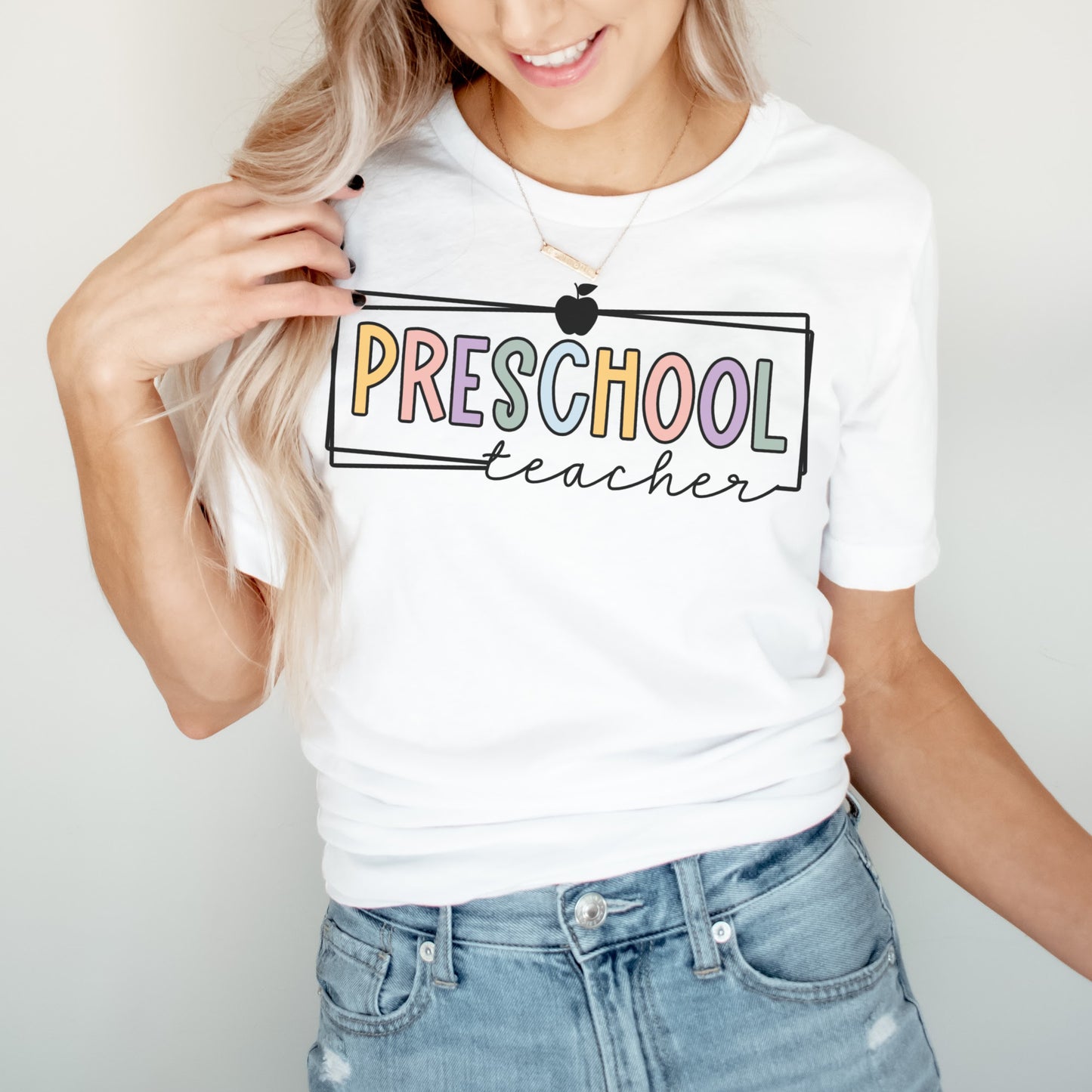 Preschool Teacher Tshirt Multicolor font with white rectangle borders and an apple on the top. White Color