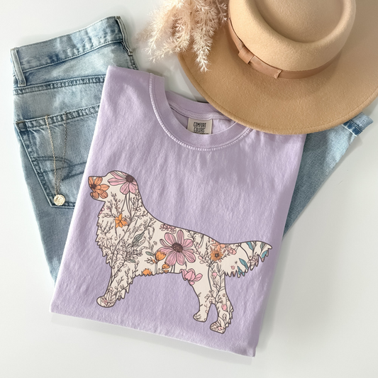 A folded unisex Comfort Colors t-shirt in orchid color featuring a silhouette of a golden retriever filled with a floral pattern of wildflowers in various colors.