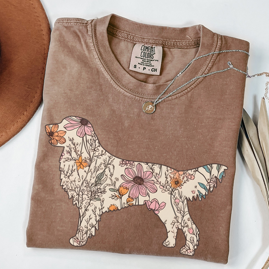 A folded unisex Comfort Colors t-shirt in espresso color featuring a silhouette of a golden retriever filled with a floral pattern of wildflowers in various colors.