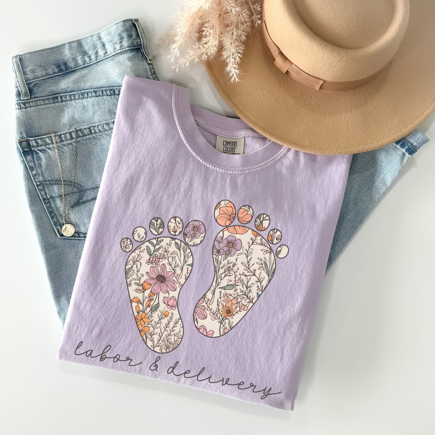 Tshirt with a graphic of two baby feet with floral design. "Labor and Delivery" in cursive underneath the footprints. Shirt Color: Orchid