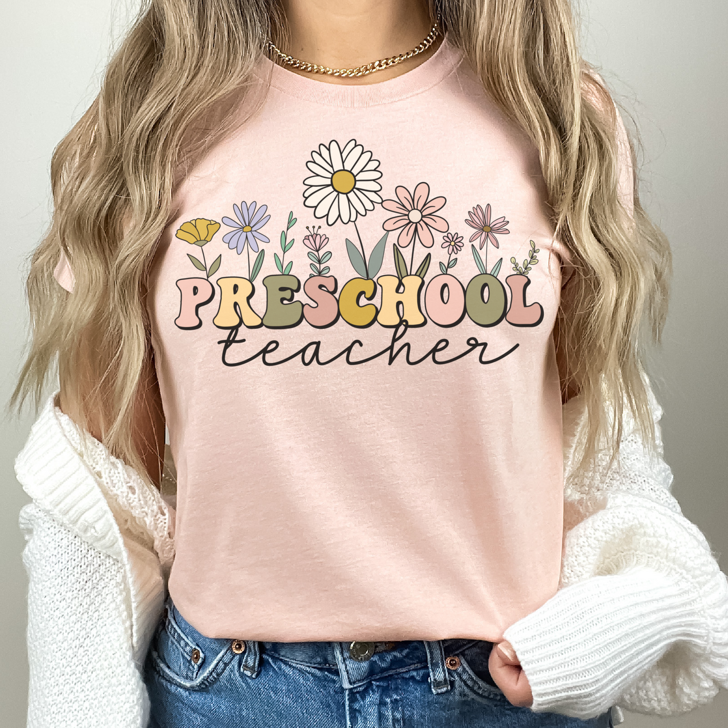 Tshirt that says "Preschool Teacher" Preschool is in a multicolored font and underneath it is 'teacher' in a black cursive text. Different colored and shaped wildflowers are coming out of the top of the word 'preschool'. Colored tshirt: heather peach